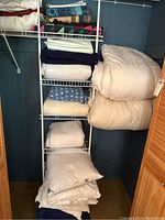 Photo of white quilted comforter, white and navy blankets, and stacked white pillows on white shelving