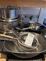 Overview of the cookware and strainers stacked together, showing various pots and a large colander on bottom.