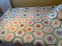 Full view of the quilt laid on the bed, showing the flower garden pattern with pastel colors and hexagonal blocks.