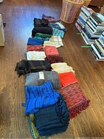 Image showing a lineup of various scarves and wraps laid out on a wooden floor next to stacks of books.