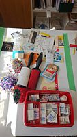 Full overview of sewing lot with needles, pin cushions, lint rollers, tape, pins and snap box on white surface