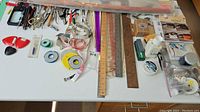 Full layout of assorted sewing tools and measuring devices on table including rulers, scissors, tape measures, sewing patterns, and various other tools.