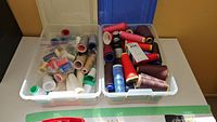 Two plastic boxes filled with assorted sewing thread spools in various colors and sizes placed on a table.