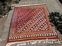 Full view of large red and brown flat-woven rug laid outdoors on pavers