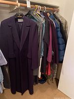 Full view of hanging winter coats and blouses in a closet, showing variety and quantity.