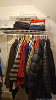 Full closet rack view showing folded sweaters on upper shelf and 12 hangers of jackets and sweaters below