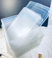 Five clear plastic storage bins stacked with lids visible, showing the size difference of the large bin compared to the smaller bins.