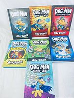 Front cover of 7 Dog Man books arranged in two rows with colorful cartoon illustrations.