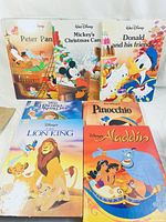 Photo showing all 7 Disney children's books arranged together on a surface: Peter Pan, Mickey's Christmas Carol, Donald and his Friends, The Hunchback of Notre Dame, The Lion King, Pinocchio, Aladdin.