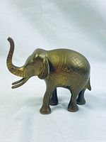 Front-left angle view of brass elephant figurine highlighting carvings and patina.