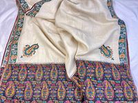 Full view of cream shawl with colorful border pattern and paisley embroidery on fabric corners.