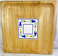 Top view of a square light wooden tray showing the smooth wood grain and inset ceramic tile with floral decorations.