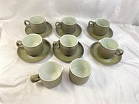 Five cups, six saucers, two creamers, and one open sugar bowl displayed on white fabric