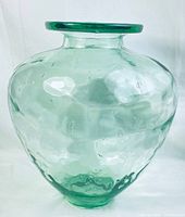 Full front view of large glass vase showing rounded body and wide flat rim, highlighting greenish tint and glass bubbles.