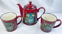 Photo shows ceramic teapot in red with owl illustrations and two matching mugs, all with matching owl-themed design.