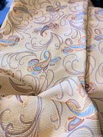 Close-up of bedspread fabric showing muted golden yellow color with pastel paisley embroidery and textured ribbed background.
