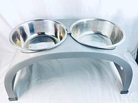 Front and side angle view of the raised feeding station showing the gray plastic stand and two stainless steel bowls.
