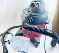 Shop-Vac wet-dry vacuum front angle showing branding, hoses attached, and reusable filter bag lying nearby.