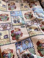 Tapestry bedspread surface showing repeating pattern of teddy bears and home scenes in checkered squares