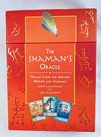 Front of the red box showing title 'The Shaman's Oracle' with feather design and images of three oracle cards, decorated with ancient symbolic art.
