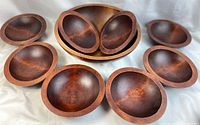 Full set view showing one large bowl surrounded by eight smaller bowls on a white cloth background, displaying the rich wood tones and polished finish.