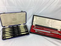 Two vintage boxed cutlery sets. Left is a Latham & Owen Sheffield cutlery set with 12 knives and 12 forks, ivory-colored handles with silver decorative ends. Right is a Birks carving set with 2 pieces in a black box with red lining.