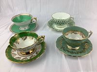 Four fine china teacup and saucer sets arranged front and center; highlights variety in color and decorative gold detailing.