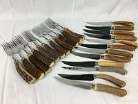 Overview of 11 knives and 12 forks laid out on white background