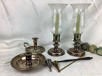 Full view of all silver plate candle holders, hurricane glass shades, and candle snuffers arranged together with measurement for scale.