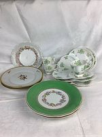Full view of assorted decorative plates and teacups showing different floral patterns and colors including green, pink, and gold accents