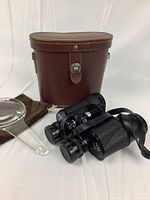 Binoculars, leather case, and magnifying glass displayed on white background