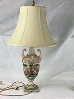 Full view of the vintage Capo-di-Monte majolica table lamp with cream fabric lampshade and detailed painted body.