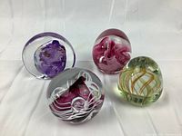 Four vintage studio glass paperweights showing front view of each with distinct internal colorful designs.