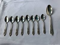 Nine sterling silver spoons arranged on white fabric background