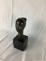 Front view of the bronze sculpture head on black marble pedestal showing the full height and form.