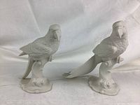 Front and side view of both white bisque porcelain parrots on their bases, showing shape and scale.