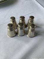 Six sterling silver salt and pepper shakers arranged in two rows of three on a white cloth surface, showing overall condition and shape.
