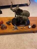 Full view of all animal and bird figurines on wooden coffee table, showing mother and baby elephant on black wooden base, cardinal bird, hummingbird with blue stones, lion pin, tiny turtle, two little pigs and additional small bird figurines
