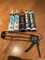 Photo of all caulking tubes and caulking tool laid out on wood floor, showing labels and condition unopened.