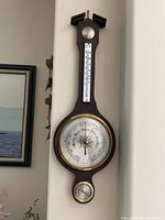 Full front view of the weather station showing the barometer, thermometer, and hygrometer on a dark wood plaque.