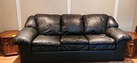 Photo showing a black leather fold-out couch with three cushions and padded arms.