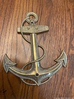 Front view of brass anchor wall decor showing rope detail and textured stock on wood surface.