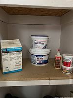 Shelf with several tubs of drywall and tiling materials, including Permacolor grout and other compounds