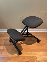 Side view of black ergonomic kneeling chair showing padded seat, knee rest, and caster wheels on wooden floor
