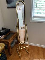 Full view of full length oval mirror on gold metal tubular stand in room, showing front view and metal stand condition