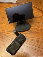 Garmin car GPS unit with a large touchscreen mounted on a stand and older handheld GPS unit with physical buttons on a wooden surface