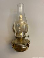 Front view of one antique wall mounted kerosene lamp showing the metal base, wick adjuster, glass chimney, and decorative metal backing plate.