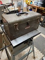 Closed metal Craftsman tool box sitting on table saw stand in basement workshop.