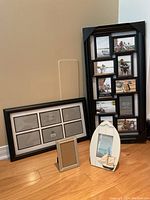 Four photo frames on floor against a wall: large frame with 10 photo openings, medium frame with 6 openings, white sailing-themed frame, and a small brown pewter frame