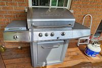 Front view of stainless steel Cuisinart barbecue grill with four main control knobs and side burner knob visible, standing on wooden deck.